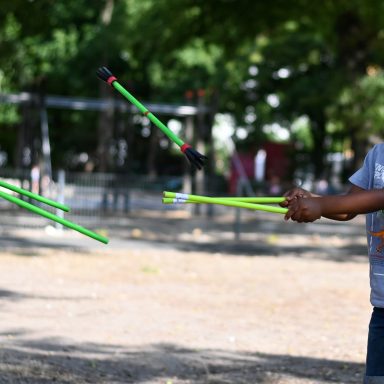 Ein Junge jongliert mit grünen Stäben im Park.