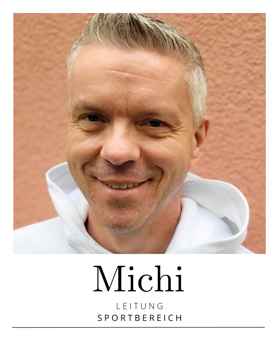 Mann mit kurzem, grauem Haar lächelt vor rosa Wand, trägt einen weißen Kapuzenpullover.