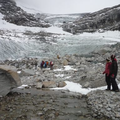 Gruppen von Menschen auf einem Gletscher zwischen Felsen und Schnee unter bewölktem Himmel.