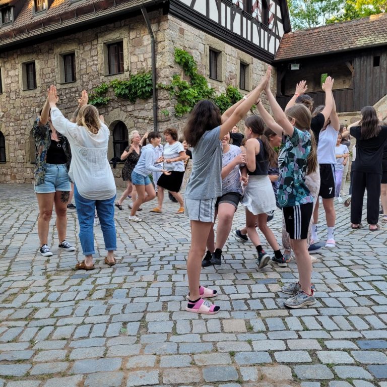 Gruppe von Kindern und Erwachsenen, die auf einem Pflasterplatz tanzen und spielen.
