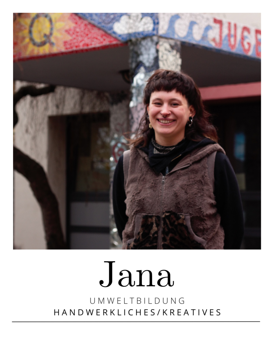 Porträt von Jana mit schwarzem Schal vor einer blauen Wand mit Fisch-Motiv.