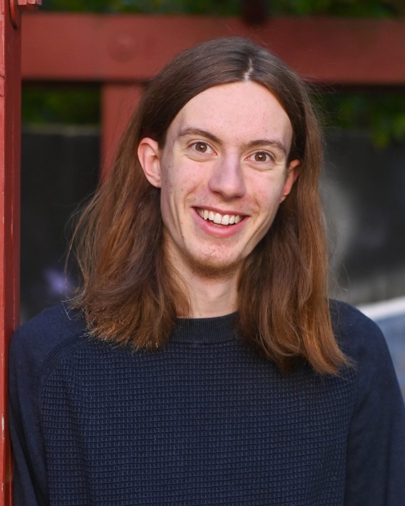 Junger Mann mit langen, braunen Haaren, braunen Augen und Lachen