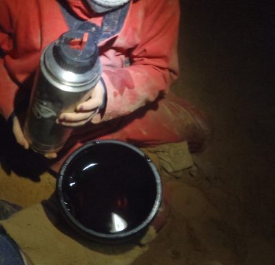 Person in roter Kleidung hält eine Thermoskanne über einen Eimer mit Flüssigkeit.
