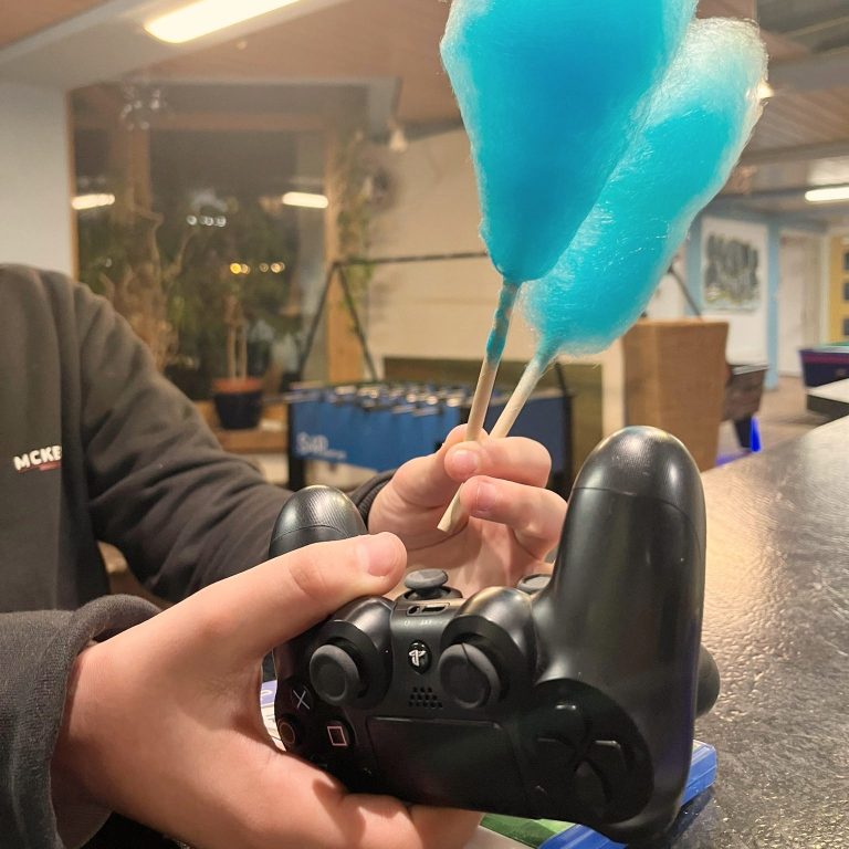 Jemand hält einen Spielecontroller und zwei Zuckerwatte-Sticks in der anderen Hand.