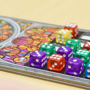 Bunte Würfel in verschiedenen Farben liegen auf einem Brettspiel mit Glasfenstern.