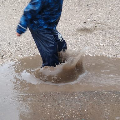 Ein Kind springt in einer Pfütze und spritzt Wasser.