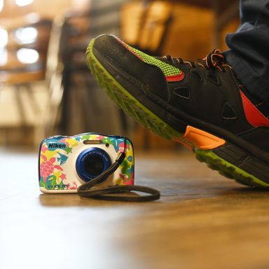 Ein bunter Kamera liegt auf dem Boden, während ein Schuh darüber steht.