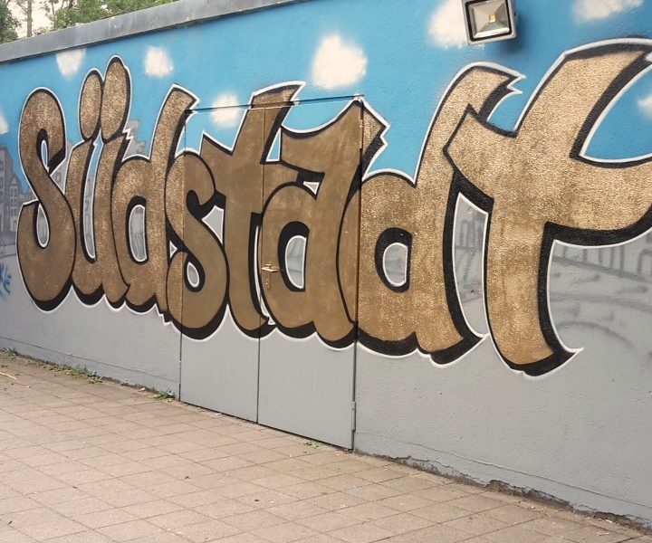 Graffiti mit dem Wort "Südstadt" in goldener Schrift vor blauem Hintergrund.