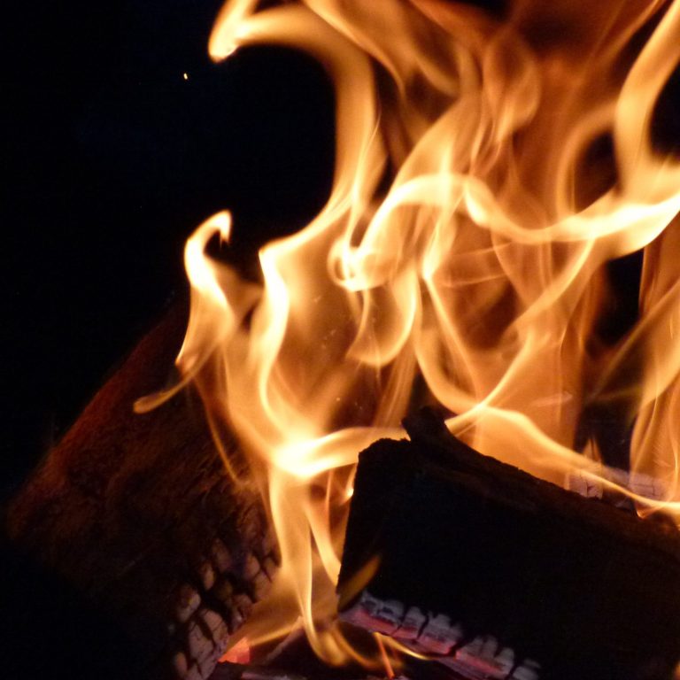 Flammen tanzen über Holzscheite in einem dunklen Hintergrund.