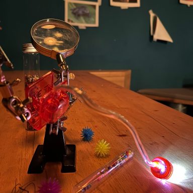 Rote mechanische Apparatur mit Glas und Licht auf einem Holztisch.