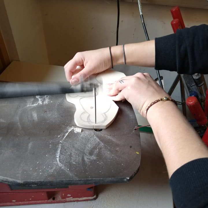 Hände formen ein Holzstück auf einer Werkbank mit Werkzeug.