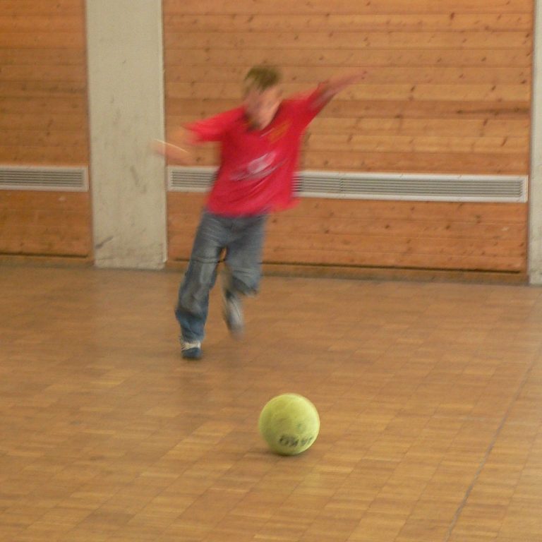 Ein Junge in rotem Shirt rennt auf einen grünen Ball zu.