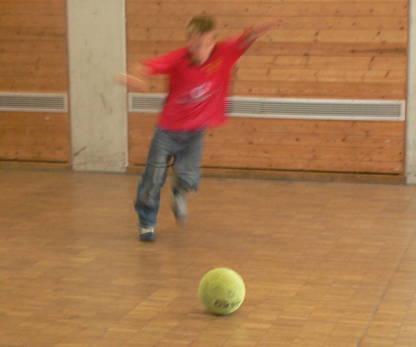 Ein Junge in rotem Shirt läuft auf einen grünen Ball zu.