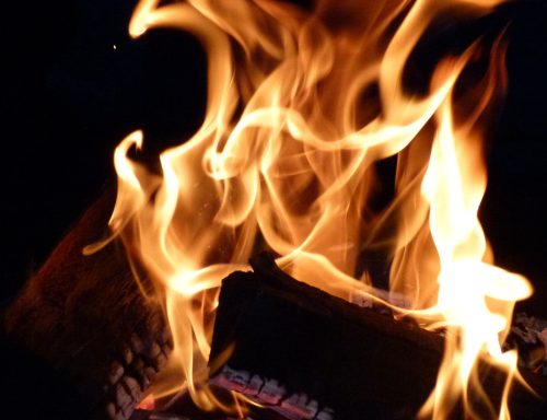 Flammen tanzen über Holzscheite in einem dunklen Hintergrund.