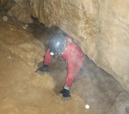 Person krabbelt in einer engen Höhle, trägt einen Helm und Handschuhe.